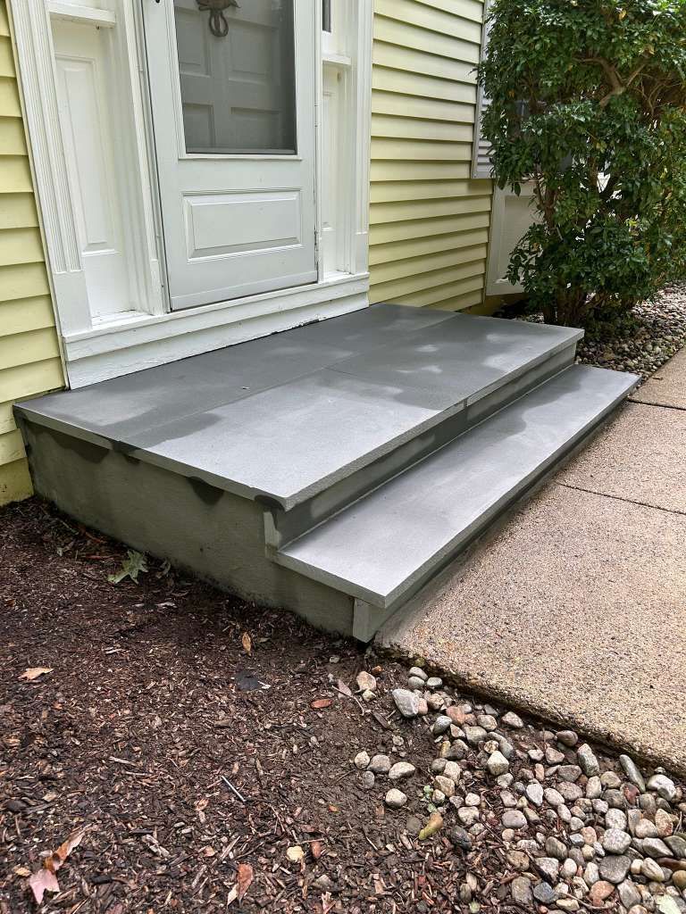 Concrete accessibility ramp leading to a front door beside a sidewalk and house siding