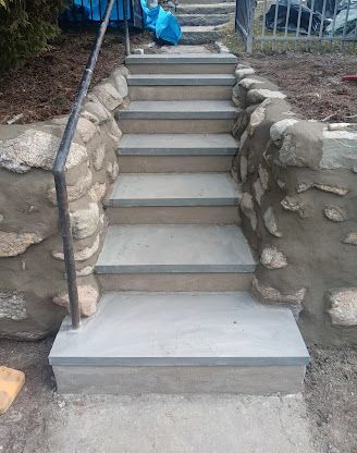 Concrete outdoor staircase with stone retaining walls and a metal handrail