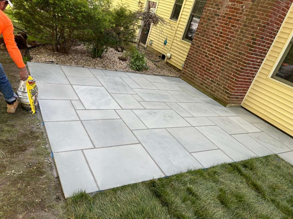 Freshly laid gray stone patio beside grass, with a worker at the left edge.