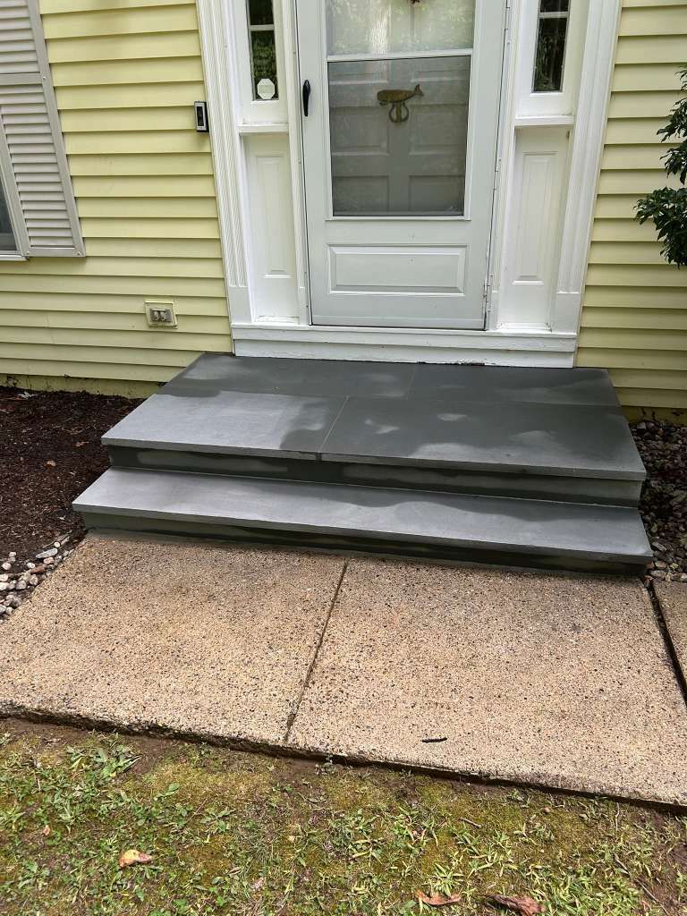 Front entry with white door and gray steps leading to a tan concrete walkway.