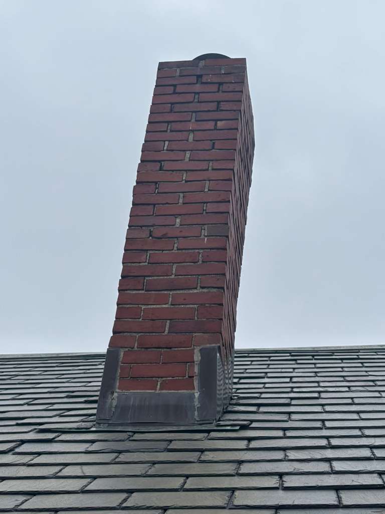 Brick chimney on a shingled roof against a cloudy sky
