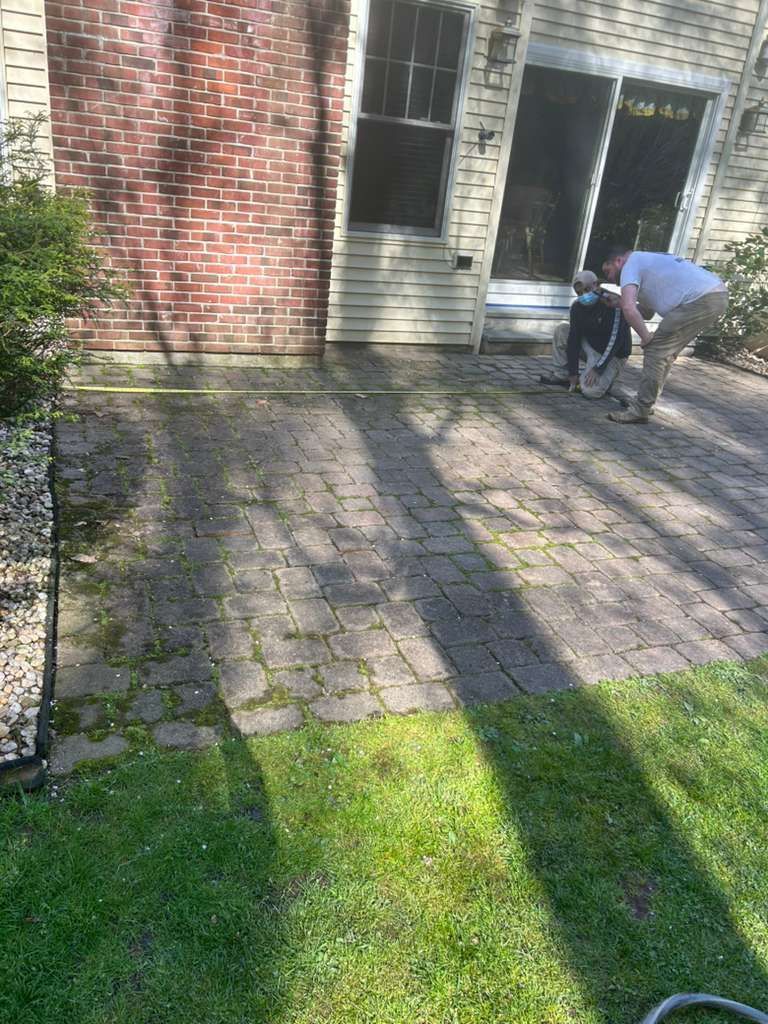 Person bending beside a black stroller on a sunlit brick patio outside a house