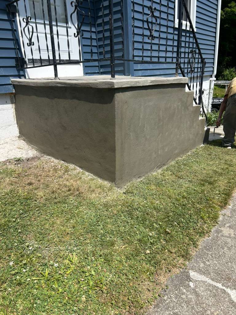 Concrete porch corner beside a house with blue siding and a small grassy yard