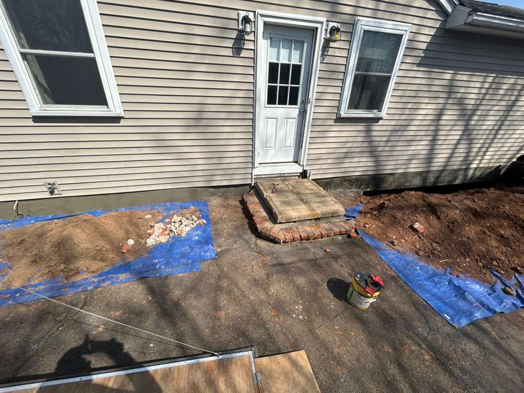 House exterior with blue tarps over soil and a brick walkway leading to a white door