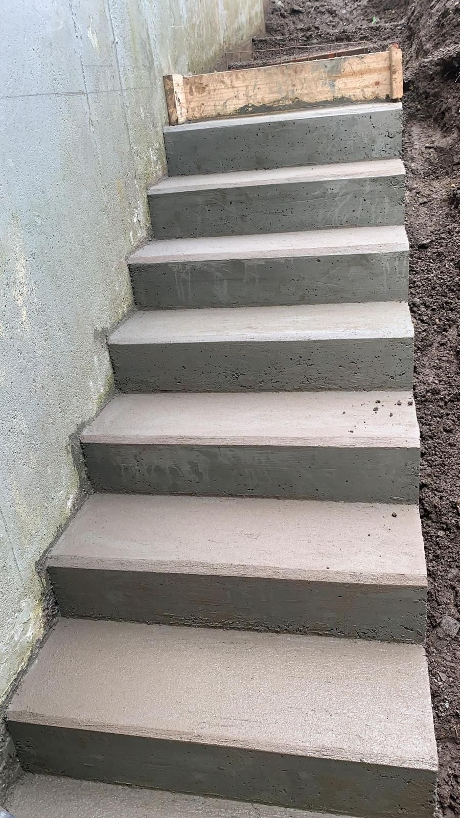 Concrete outdoor staircase with gray steps between a wall and dirt slope