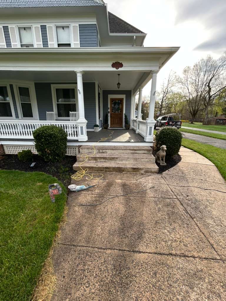 Front porch entrance of a gray house with steps, white columns, and a curved concrete driveway.