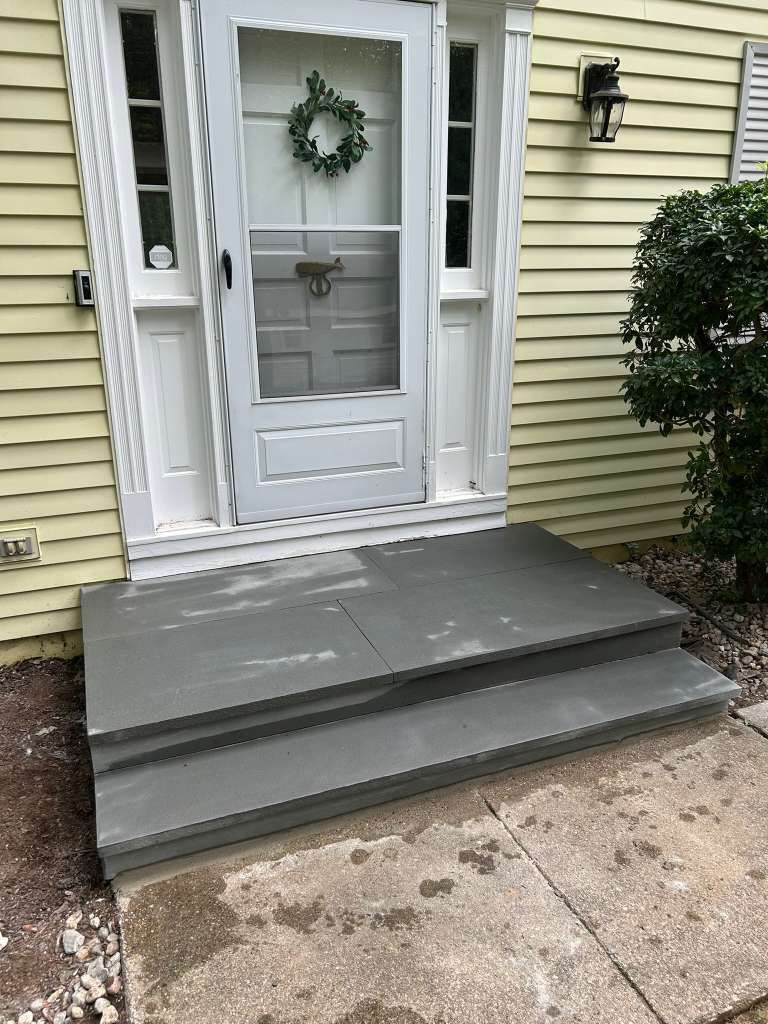 Front entry with gray accessibility ramp and steps leading to a white door on a yellow house.