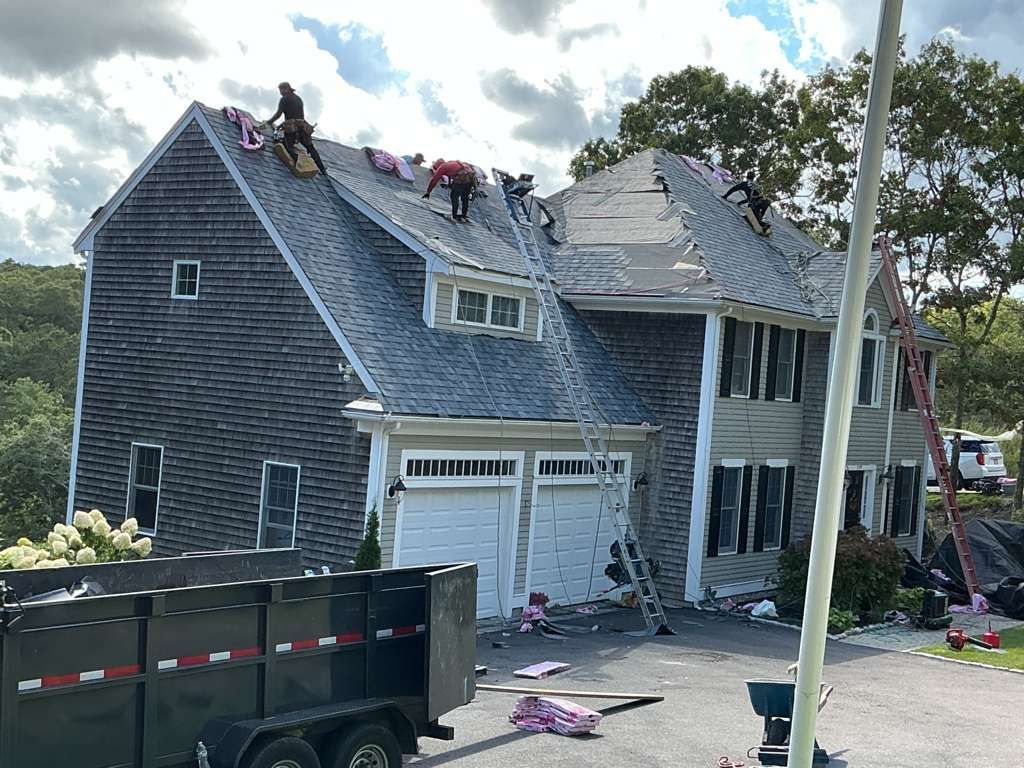Workers repair damaged gray house with roof damage and debris in the driveway