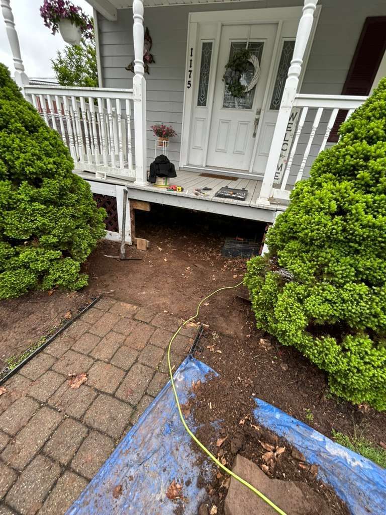 Front porch with white columns and a damaged dirt patch where walkway bricks are removed.