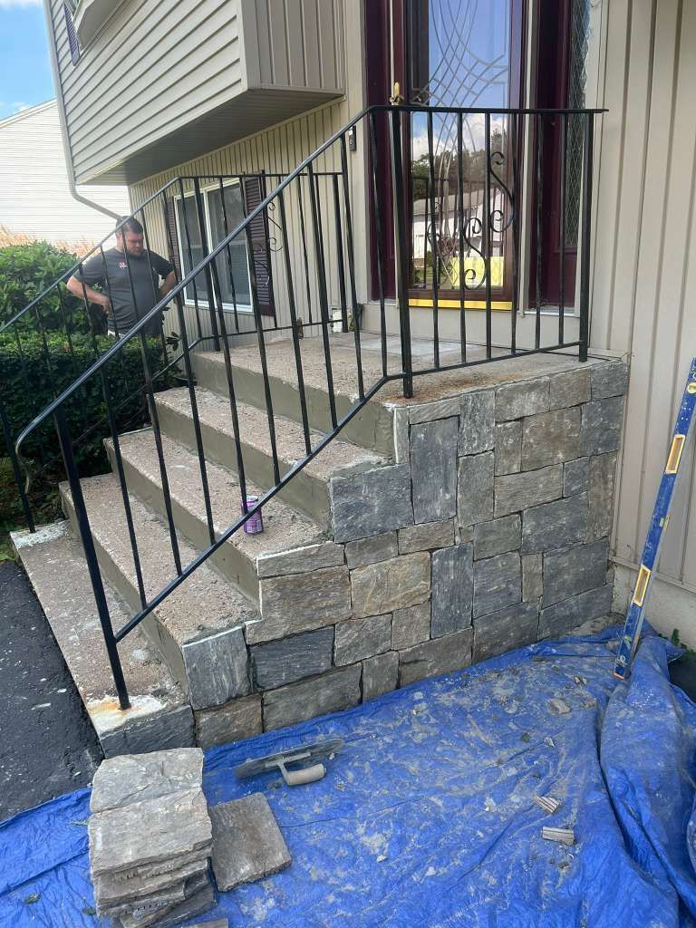 Stone stairway under construction with black railing, blue tarp, and a worker at left