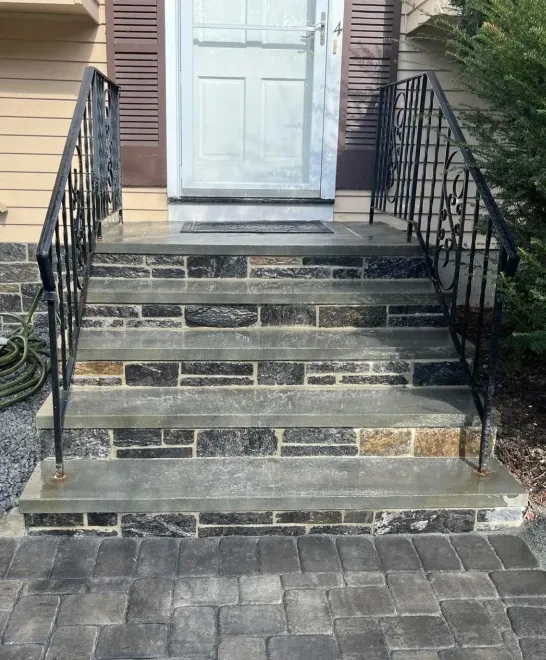 Front steps with black iron railings leading to a white door and a paved entryway.