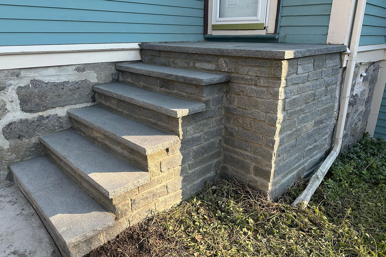 Concrete steps leading to a blue house with stone foundation and a small grassy yard.