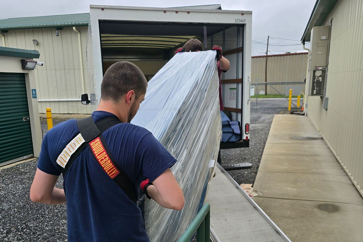 Two people loading a large wrapped item into a truck beside a building