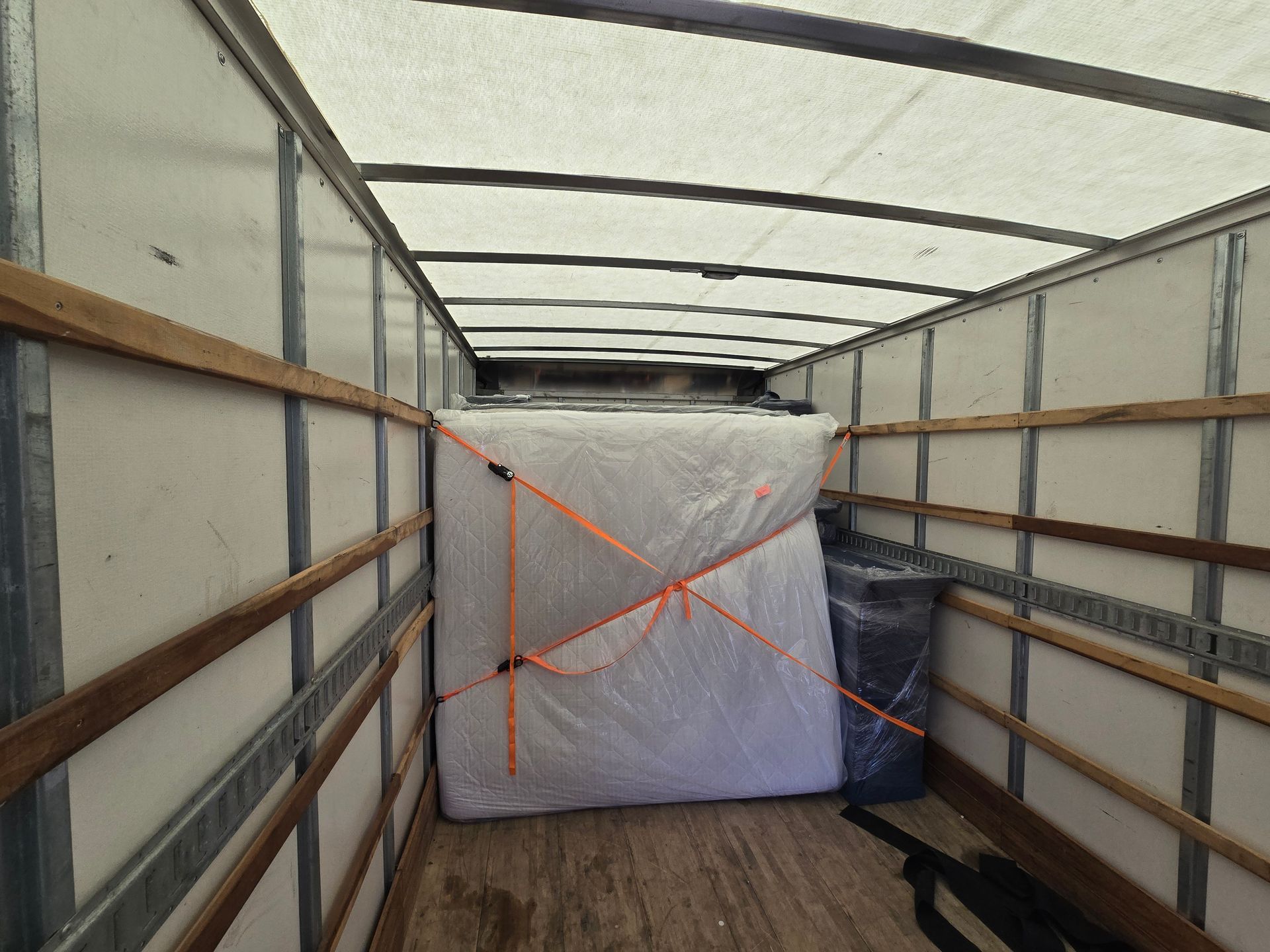 Large wrapped package secured with orange straps inside an empty truck trailer.