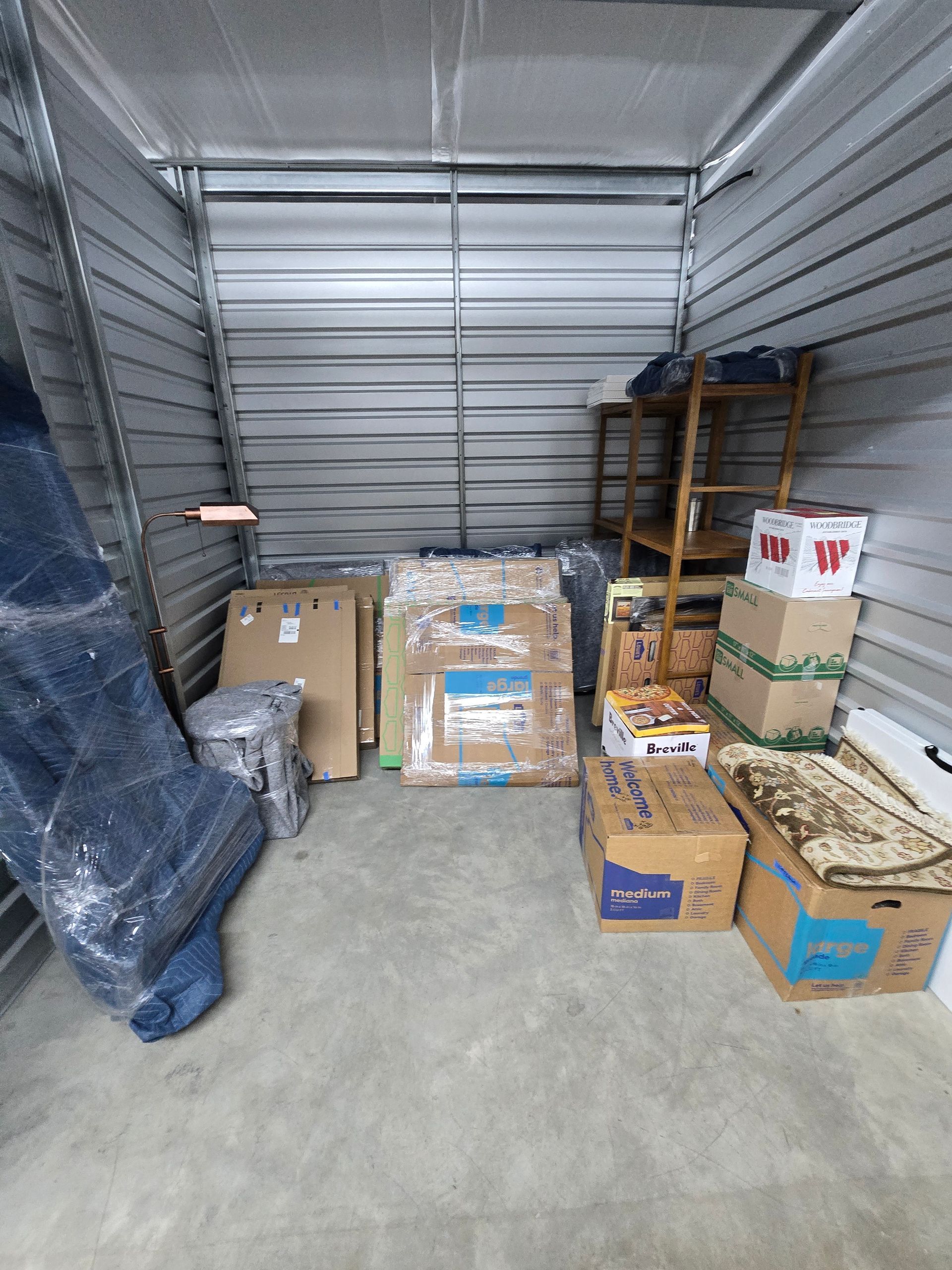 Storage unit with stacked cardboard boxes, a rolled blue tarp, and shelves against metal roll-up doors.