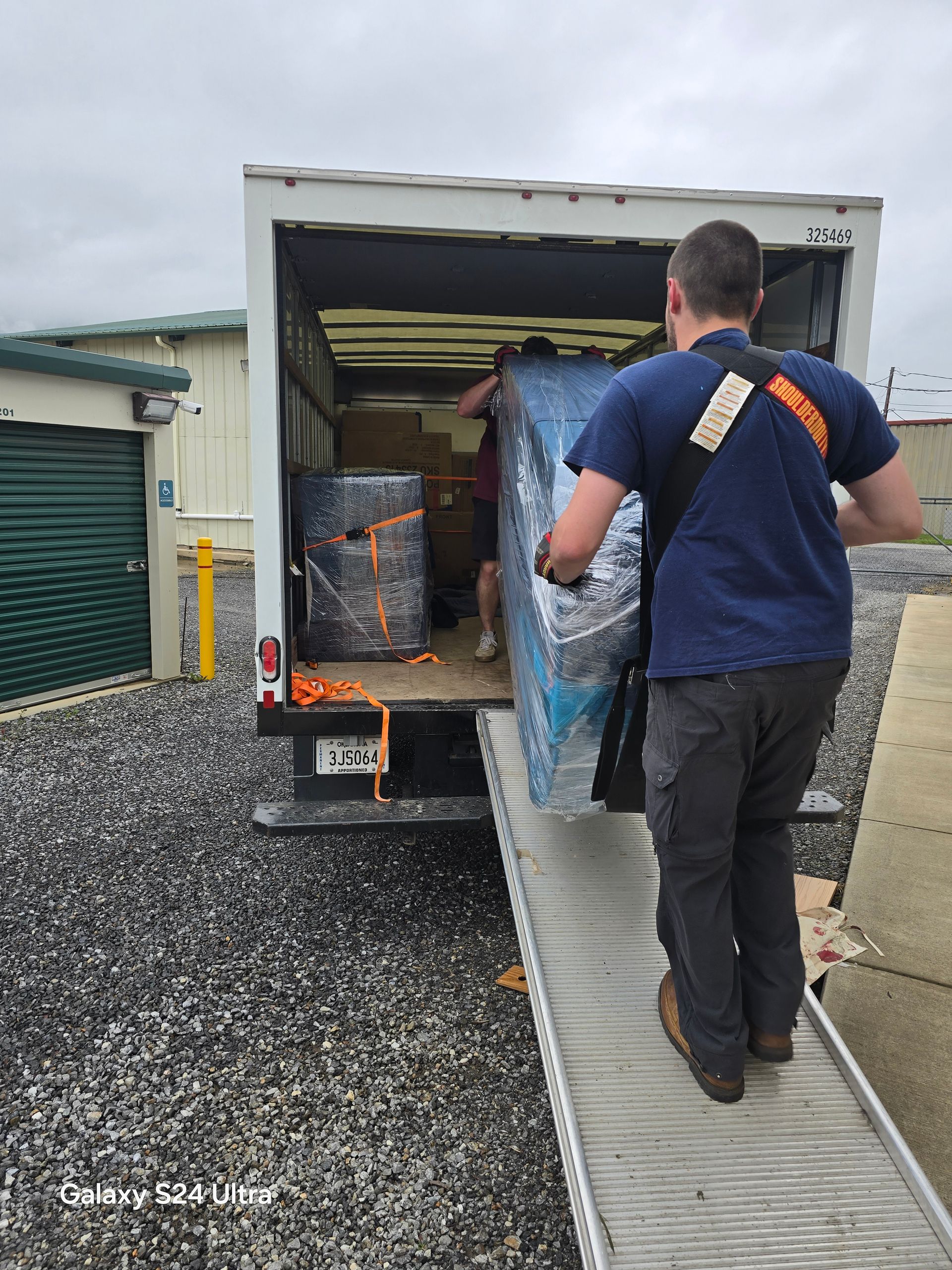 Worker carrying materials up a ramp into a box truck at a gravel storage site