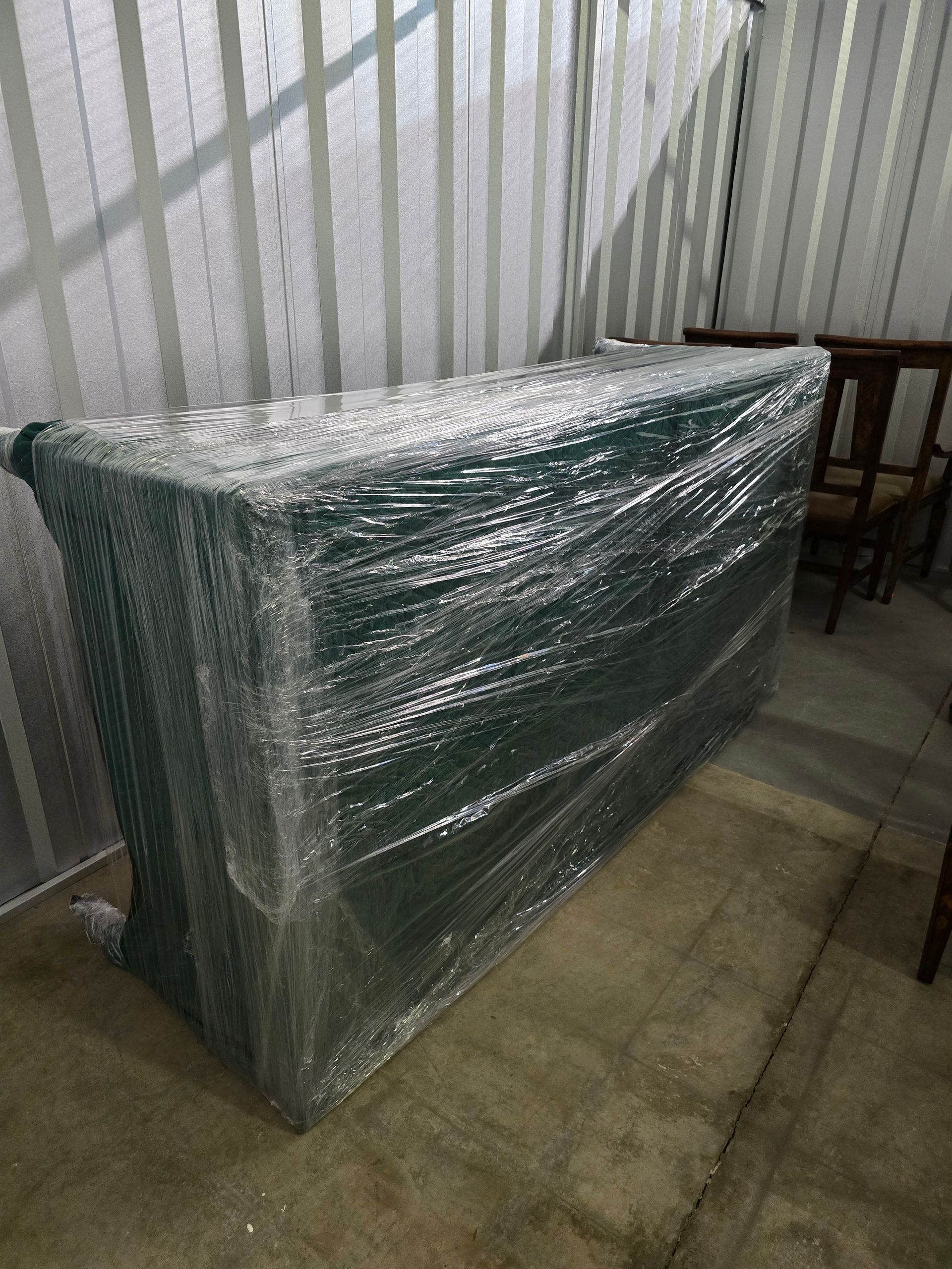 Wrapped green furniture leaning against a wall in a room with tiled floor and chairs nearby
