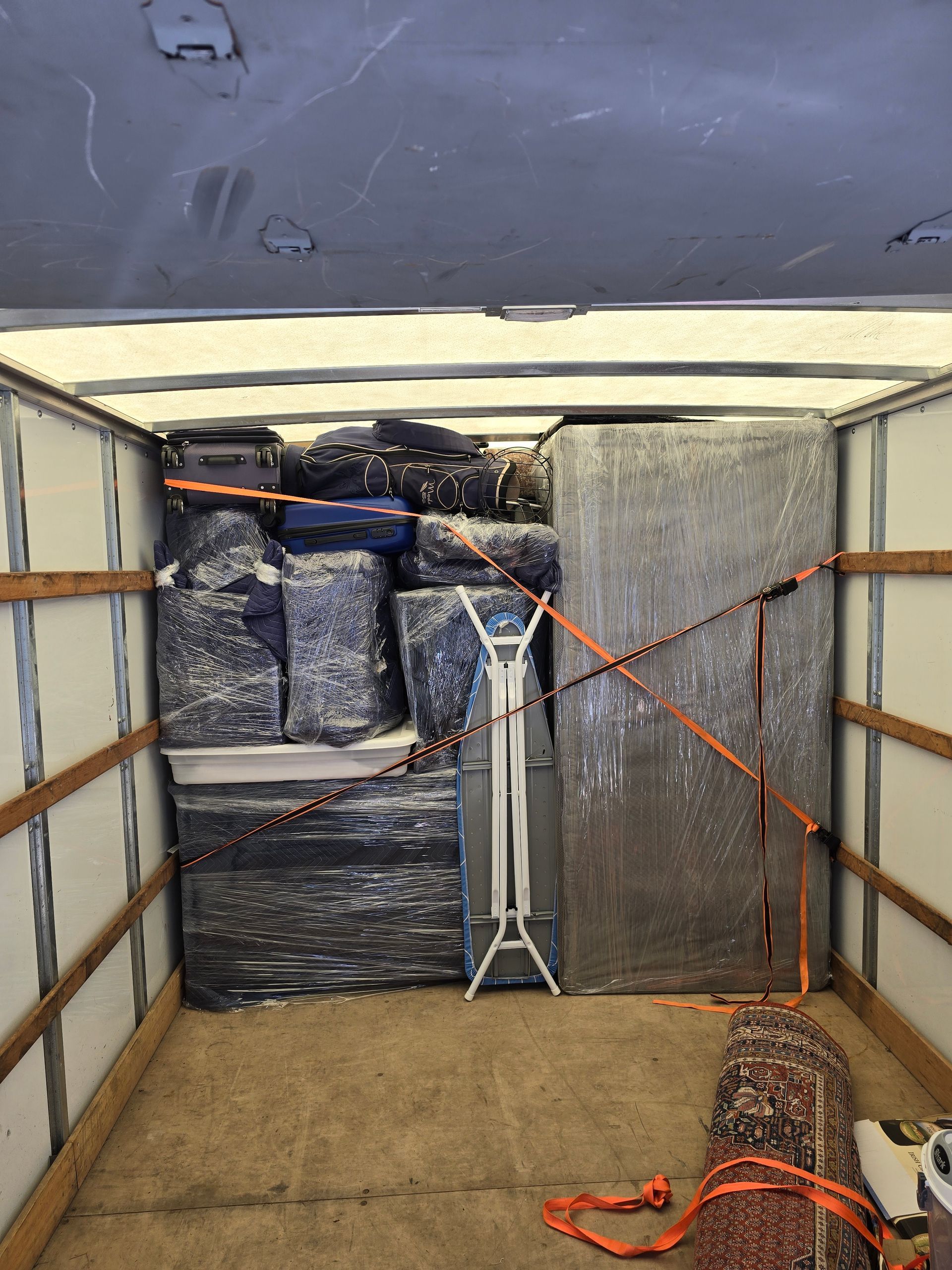 Cargo truck interior with wrapped pallets, a tripod stand, and orange tie-down straps on the floor