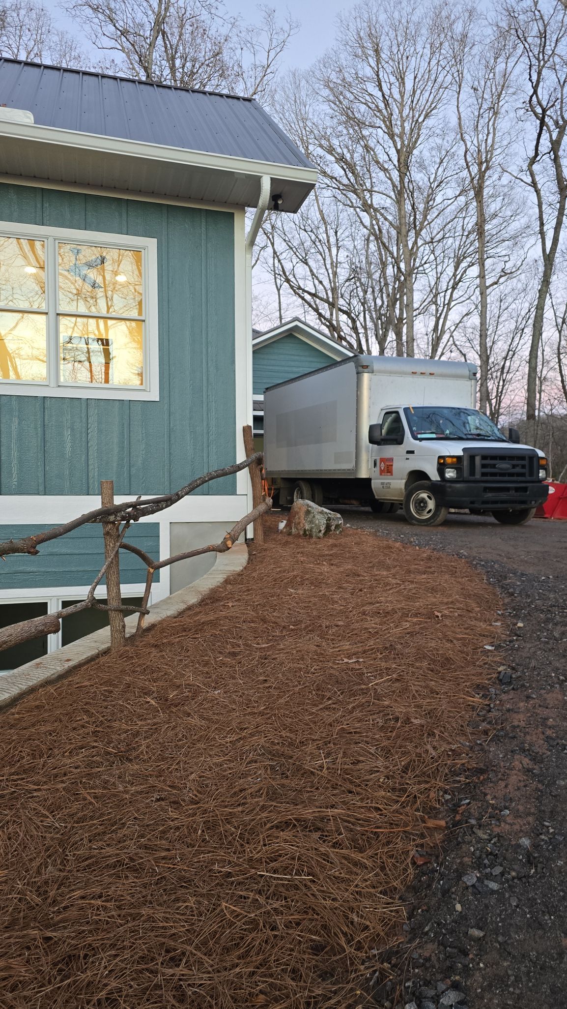 White box truck parked beside a blue house with a snowy yard and leaf-covered ground