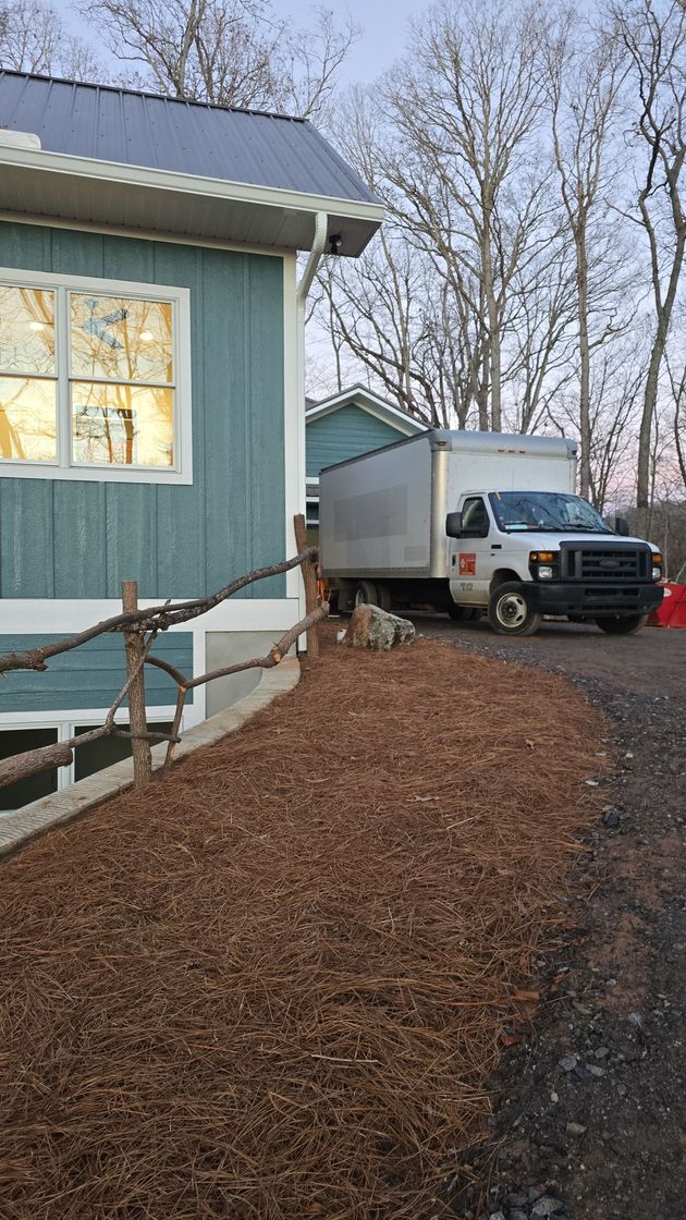 White house with blue trim beside a parked white box truck along a leaf-covered driveway.