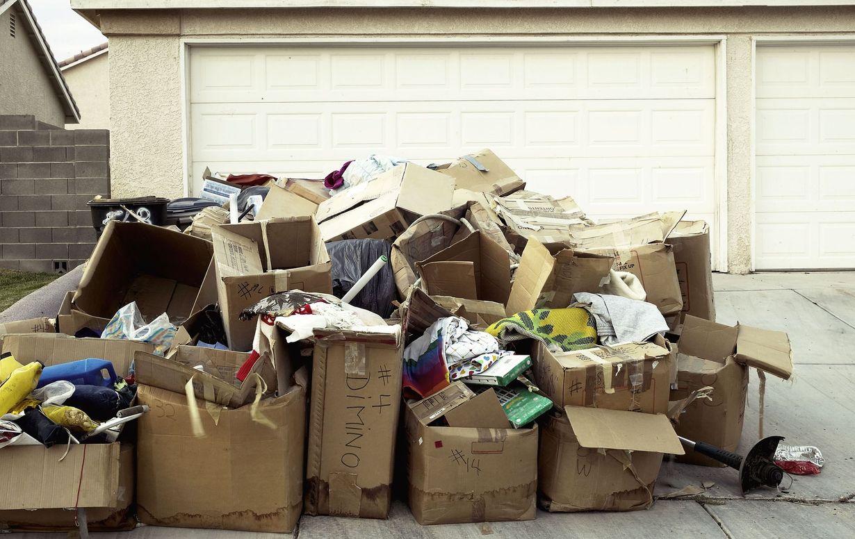 Overflowing pile of cardboard boxes and trash bags stacked in front of a garage