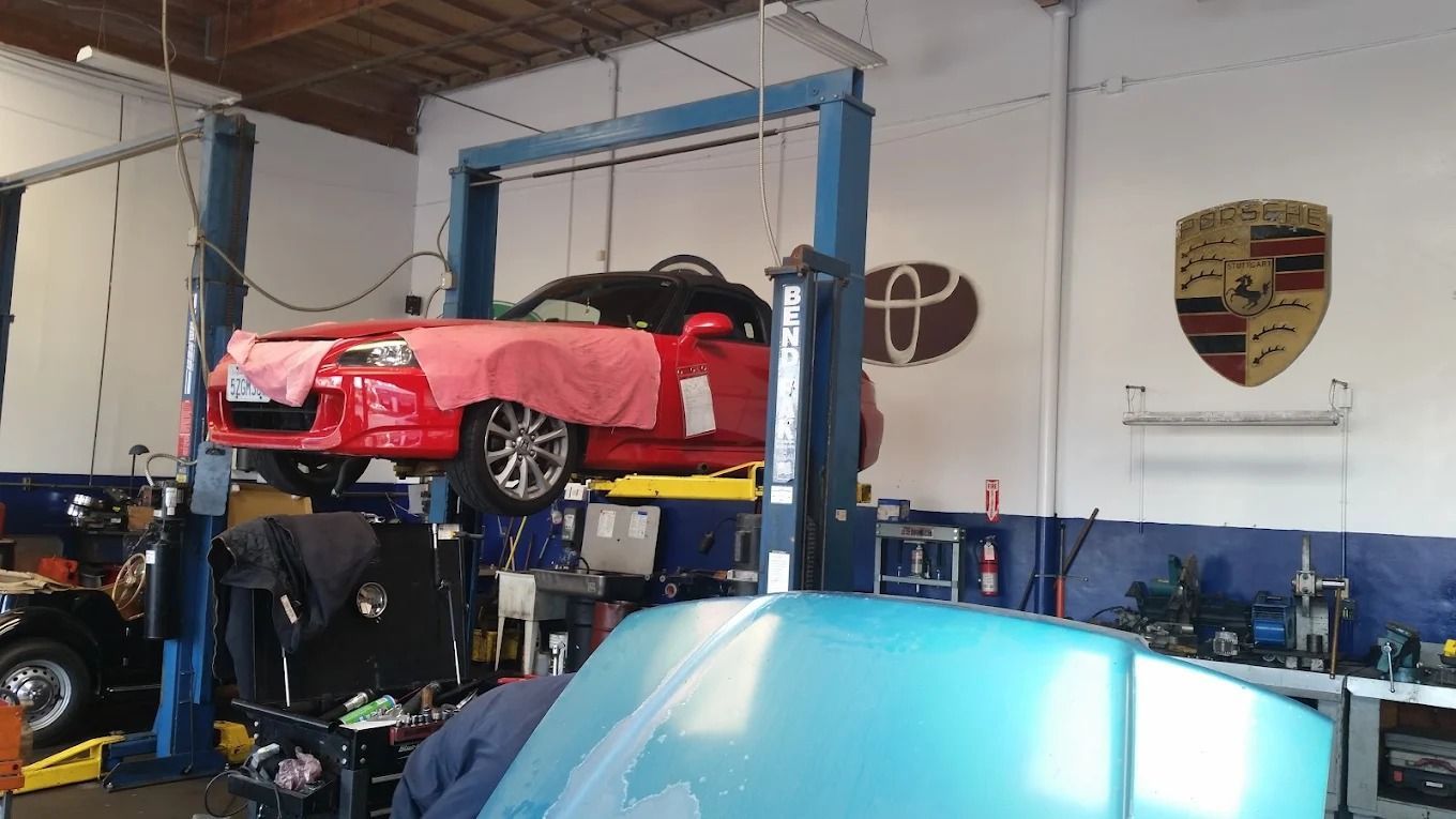 Red sports car on a lift inside an auto repair shop, with a blue car hood in the foreground.