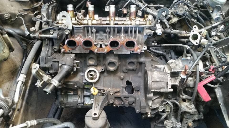 Disassembled car engine block with hoses, bolts, and metal parts laid out in a repair workspace