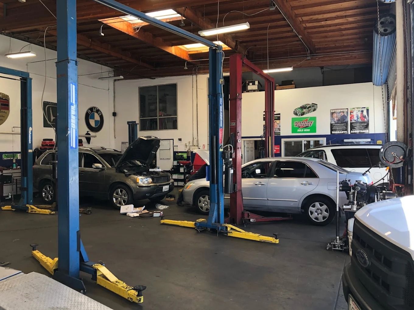 Auto repair shop with several cars on lifts and the floor, viewed inside a garage bay.
