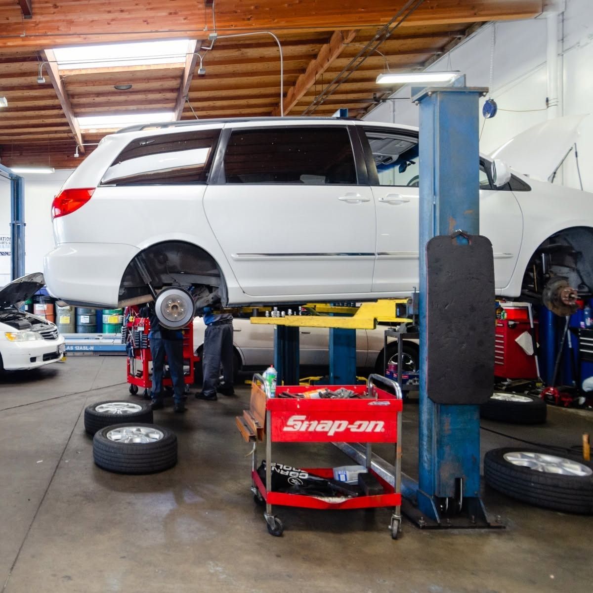 White SUV lifted in auto repair shop with wheels removed and tools on the floor
