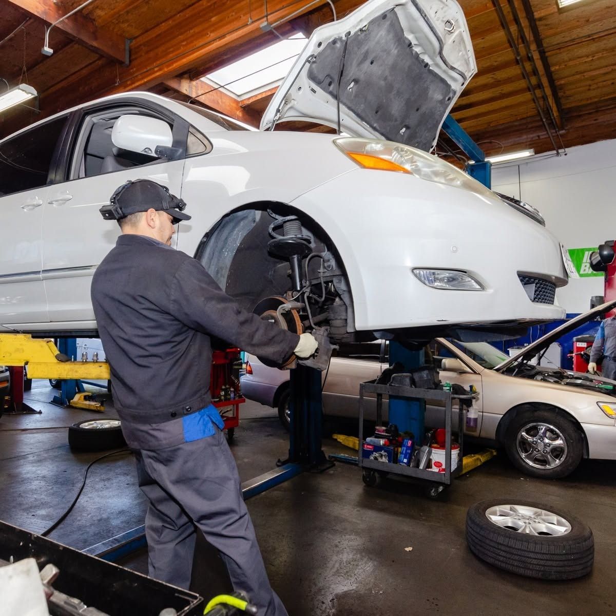 Mechanic repairing the front wheel of a white car on a lift in an auto shop