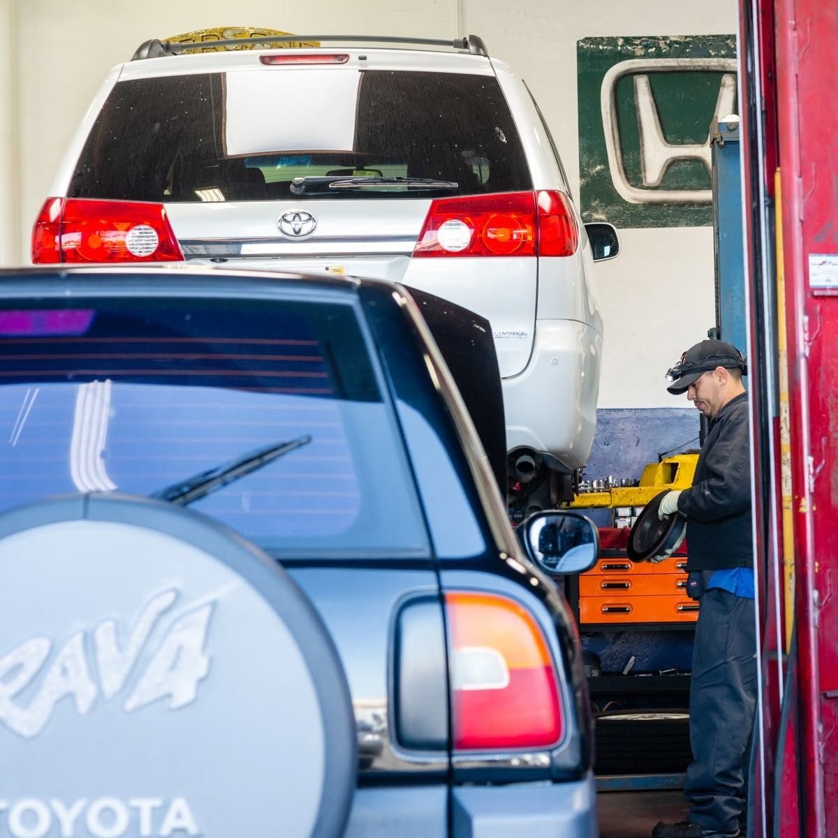 Vehicles stacked in a garage, with a mechanic working beside a white SUV on a lift.