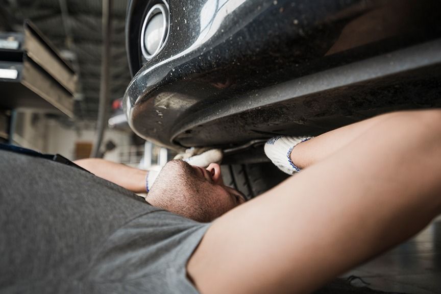 Person kneels beside a car, using a wrench underneath the front bumper.