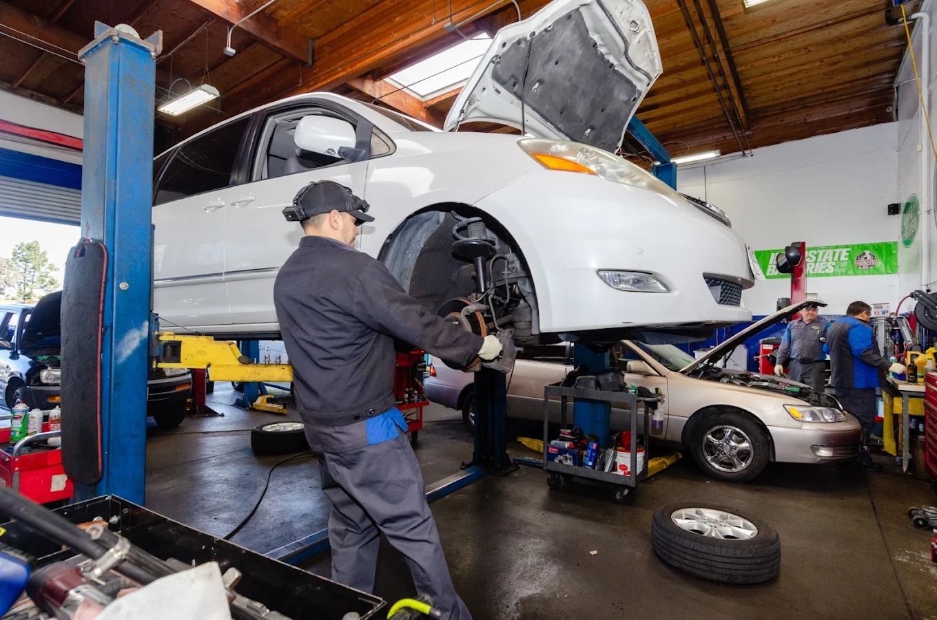 White car raised on a lift in an auto repair shop, with a mechanic working underneath.