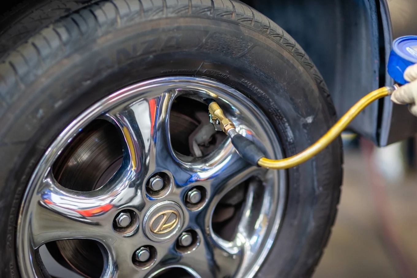 Car tire being inflated with an air hose, showing a chrome wheel and valve stem