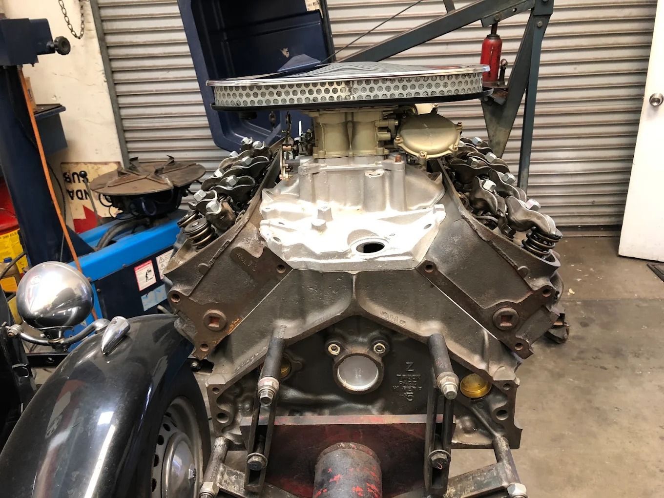 Large V8 engine mounted in a garage, with black side pipes and exposed intake components