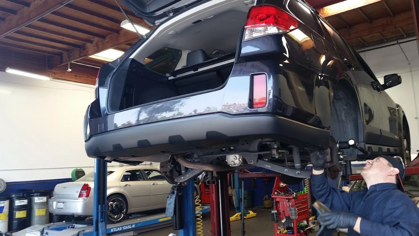 Black SUV raised on a lift in a garage while a mechanic works underneath