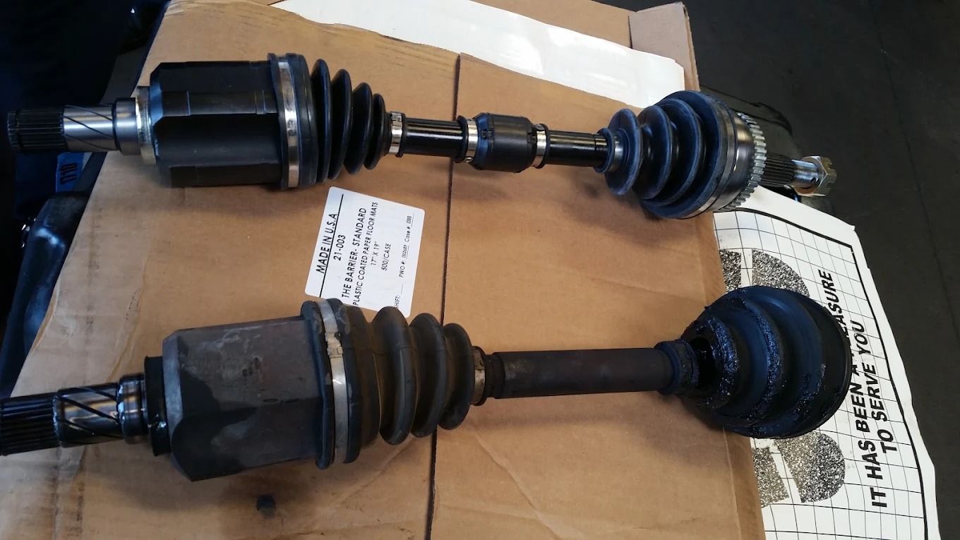 Two car CV axle shafts with black rubber boots laid on cardboard.