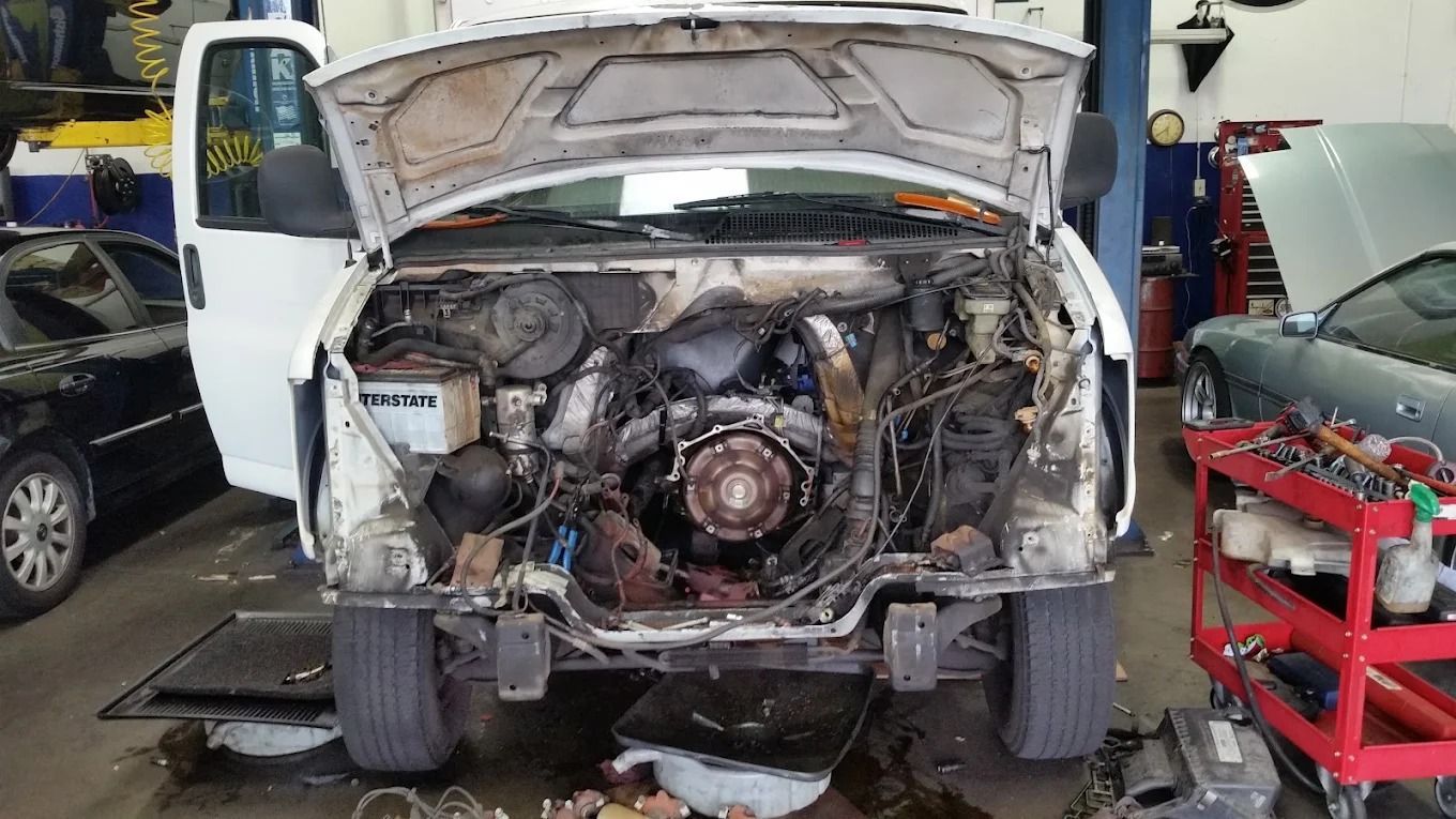 White van in an auto shop with its front body removed, exposing the engine bay during repair.