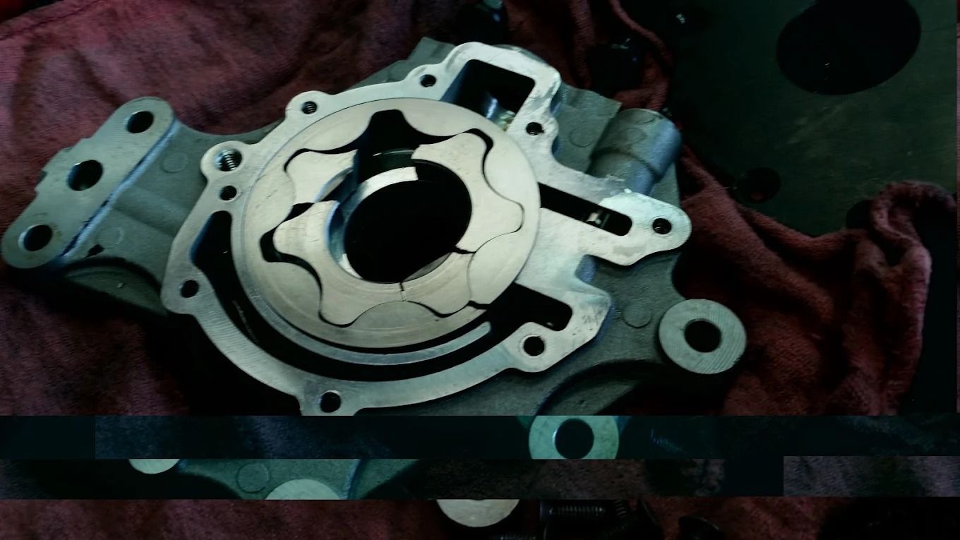 Metal mechanical part with a central opening and bolt holes, resting on a dark red cloth.