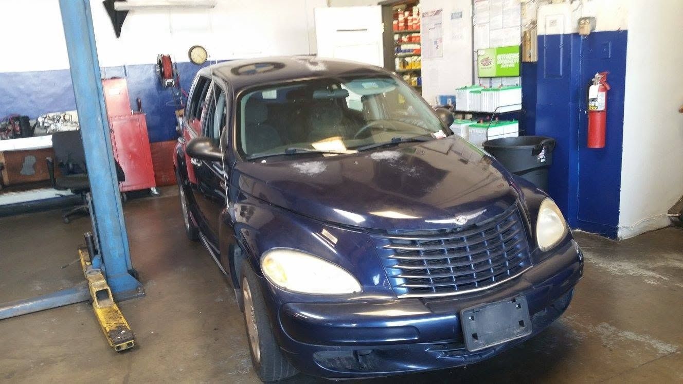 Blue car in an auto repair garage on a lift, surrounded by tools and equipment.
