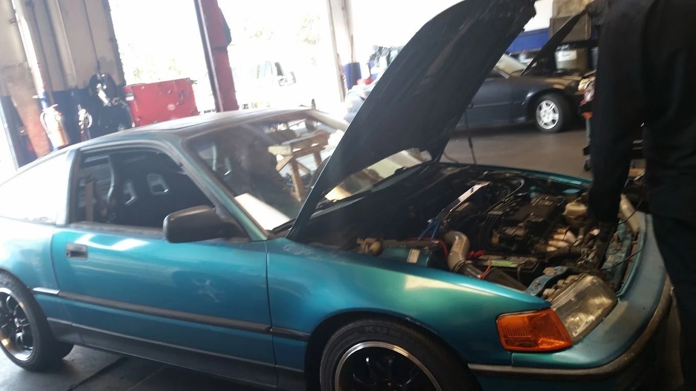 Teal sedan with hood open in a garage, showing engine bay during maintenance.