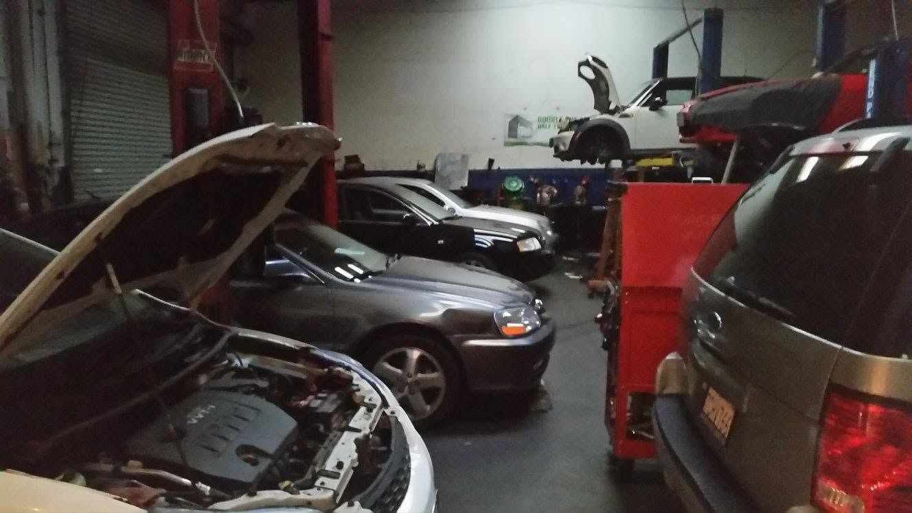Cluttered auto repair garage with several cars, one hood open in the foreground, and tools in the background