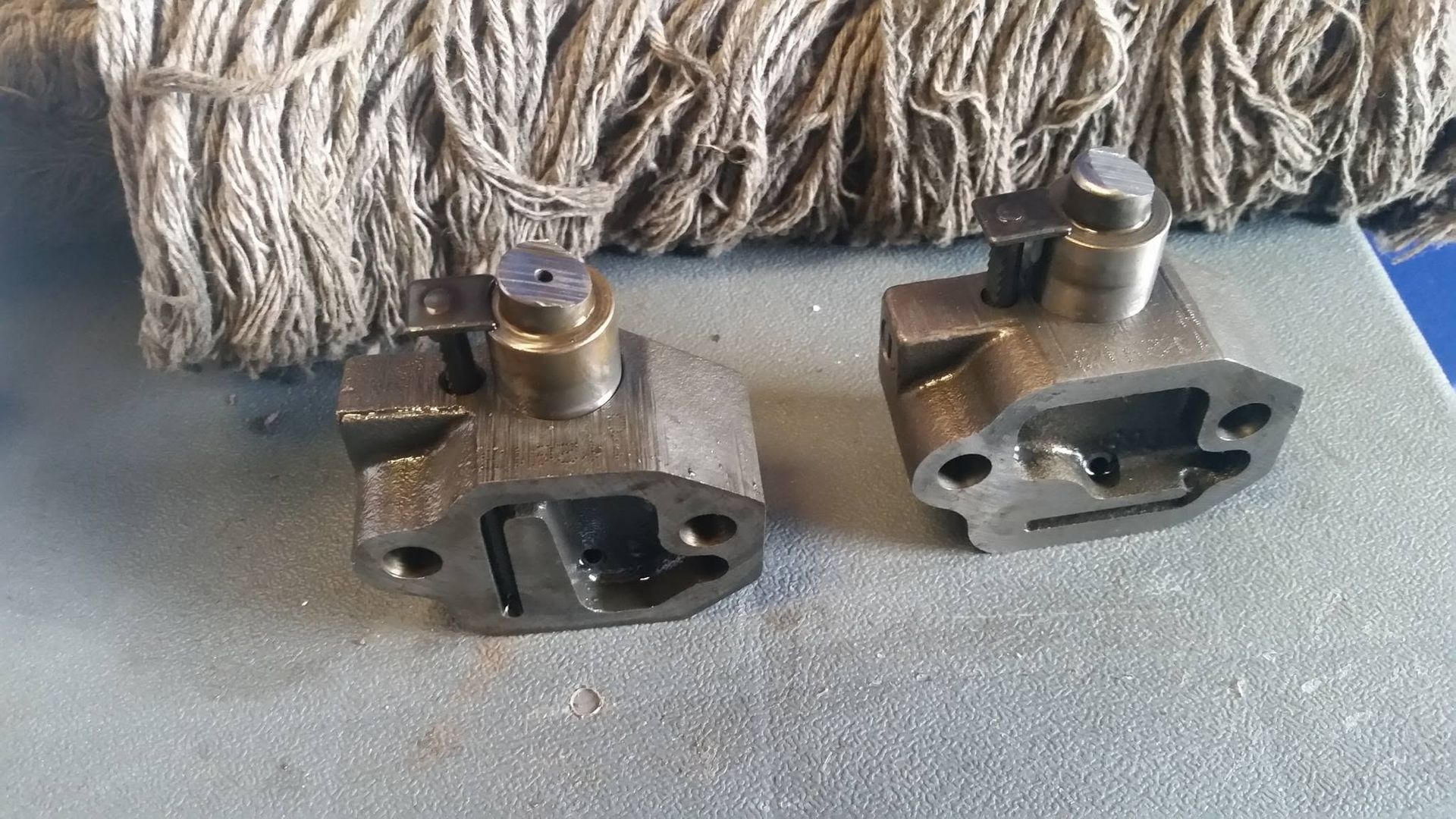 Two metal mechanical clamps with bolts, resting on a gray surface in front of a frayed fabric background