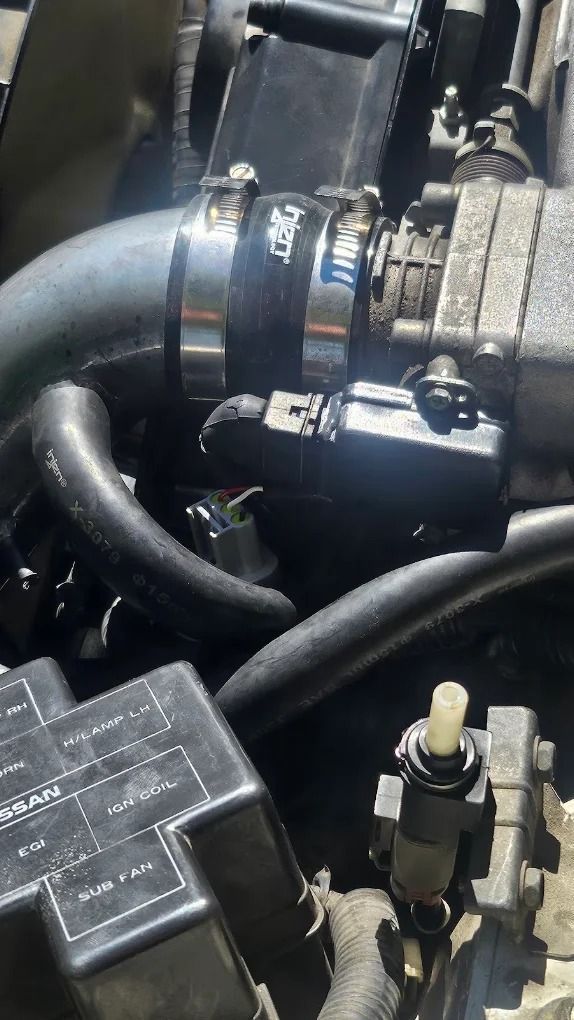 Close-up of a car engine hose connected to a metal pipe with a clamp and nearby electrical components