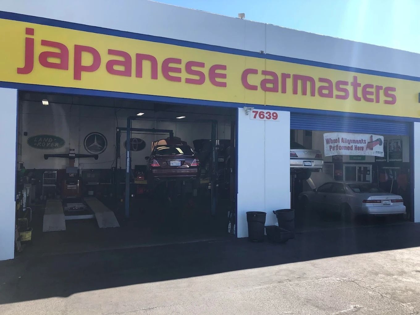 Car repair shop storefront with a yellow-and-purple “Japanese Car Masters” sign and cars inside the garage.