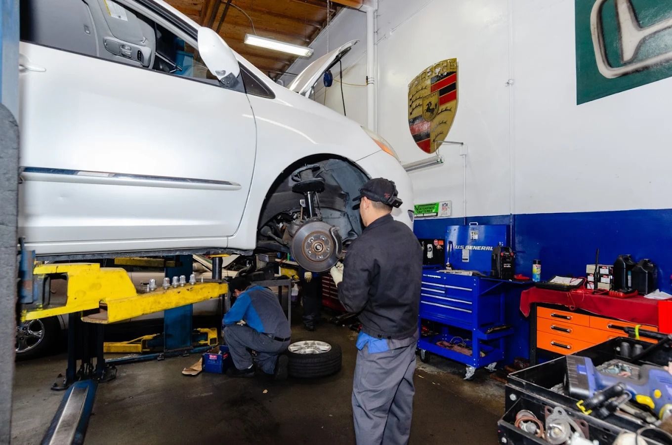 Mechanic working under a raised white SUV in an auto repair shop with blue tool cabinets