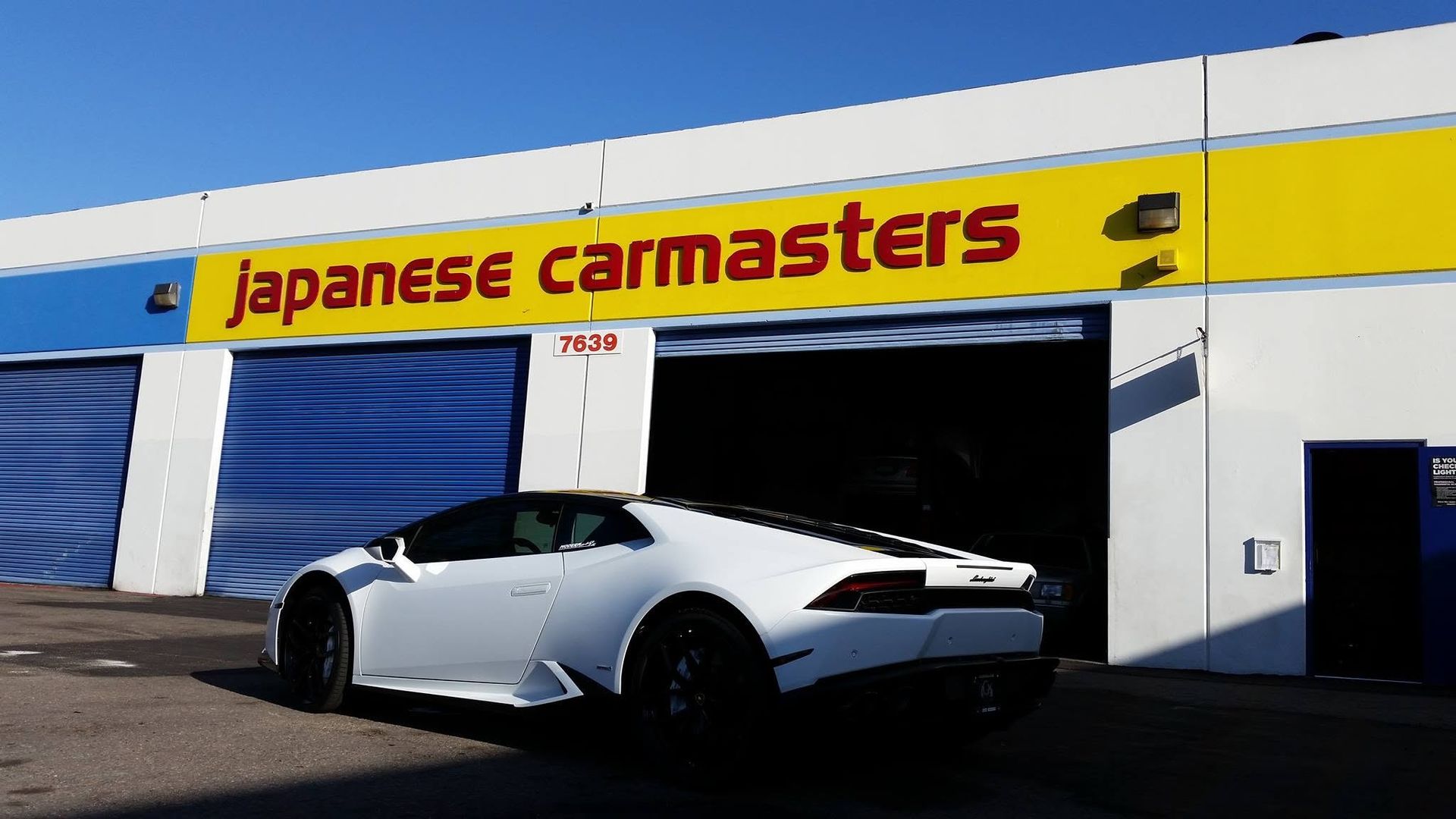 White sports car outside Japanese Carmasters auto shop with yellow sign and blue garage doors