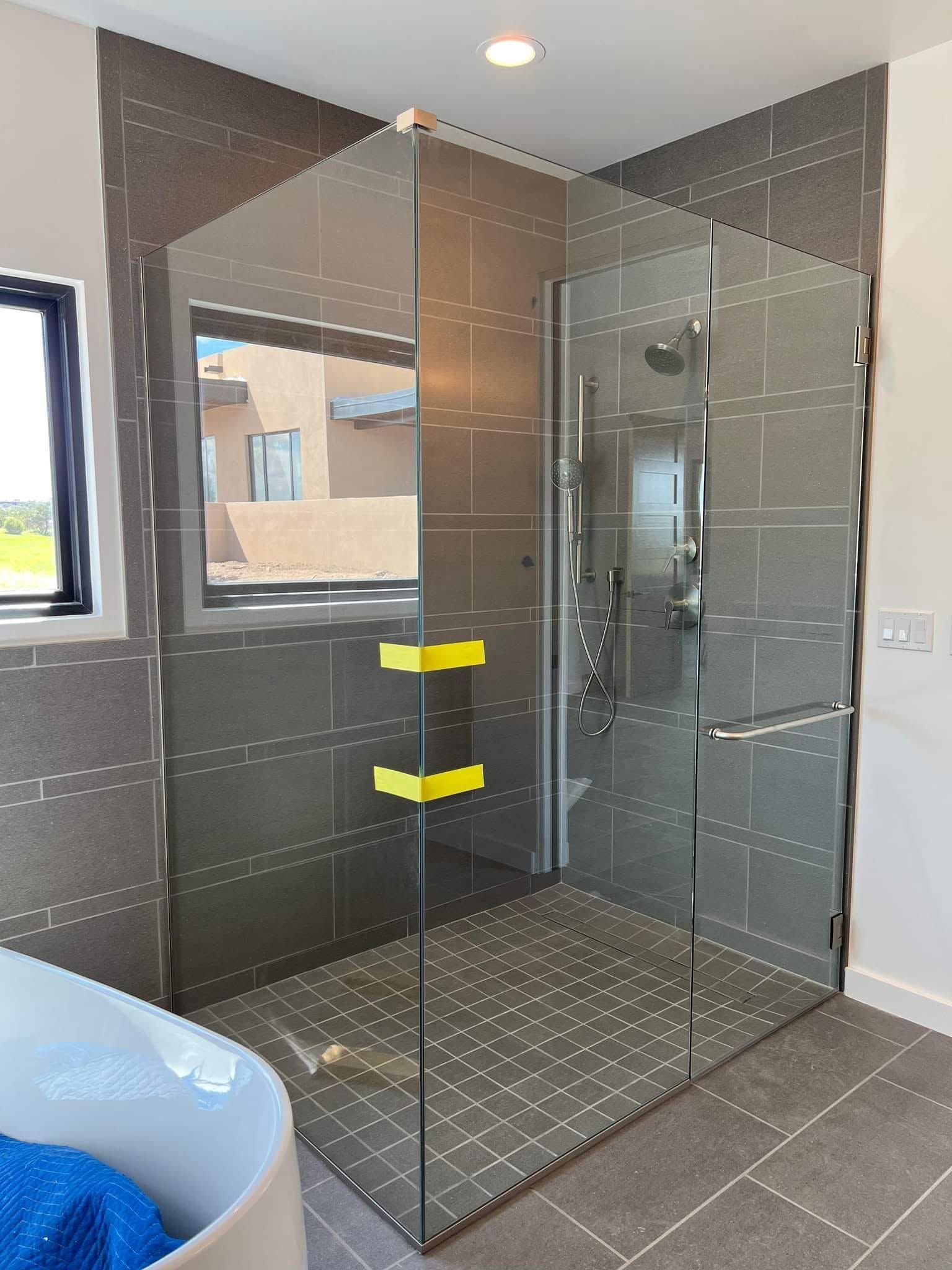 Glass shower enclosure in a modern bathroom with gray tile and yellow handles.