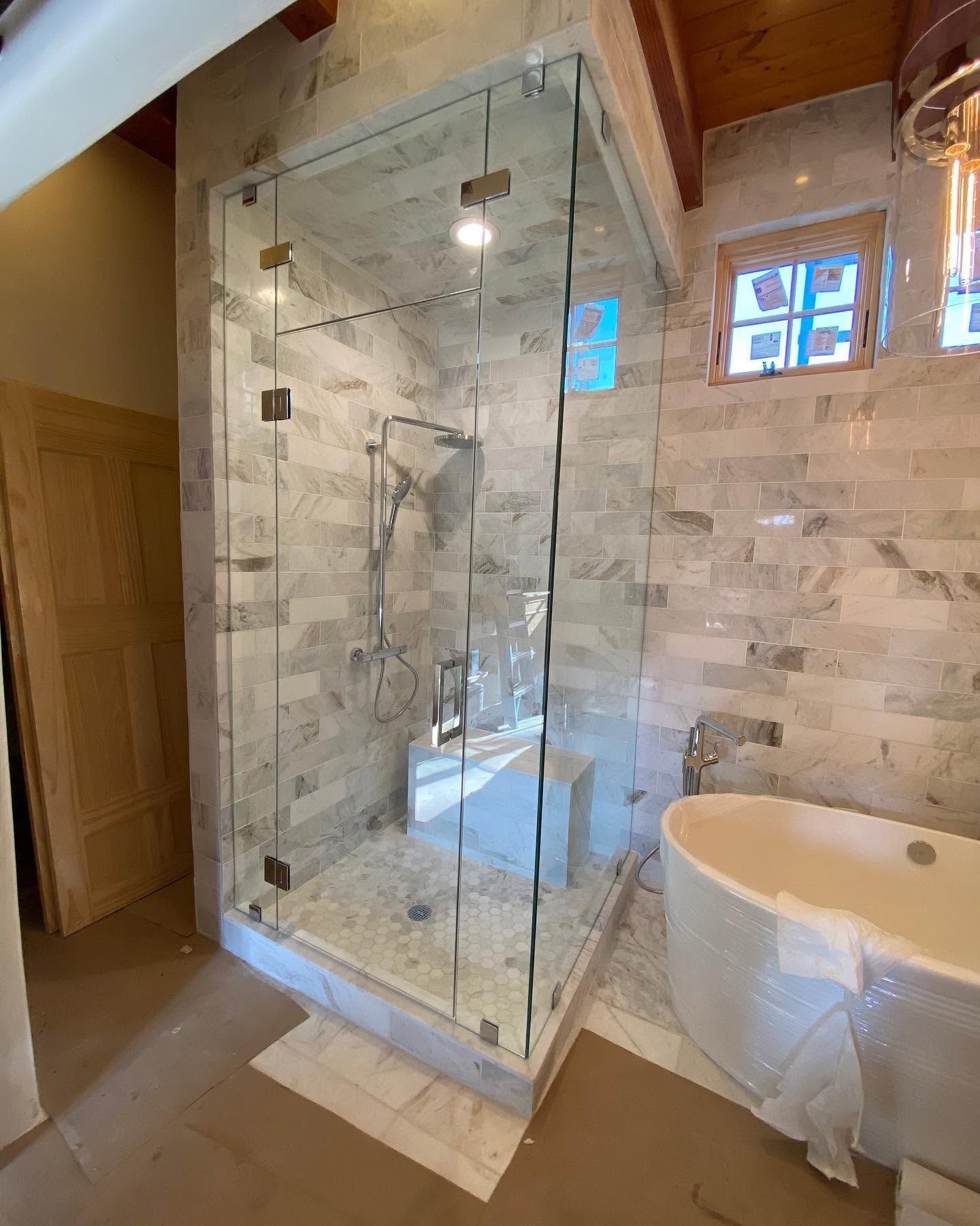 Modern bathroom with glass shower, marble tile walls, and freestanding tub next to a window.