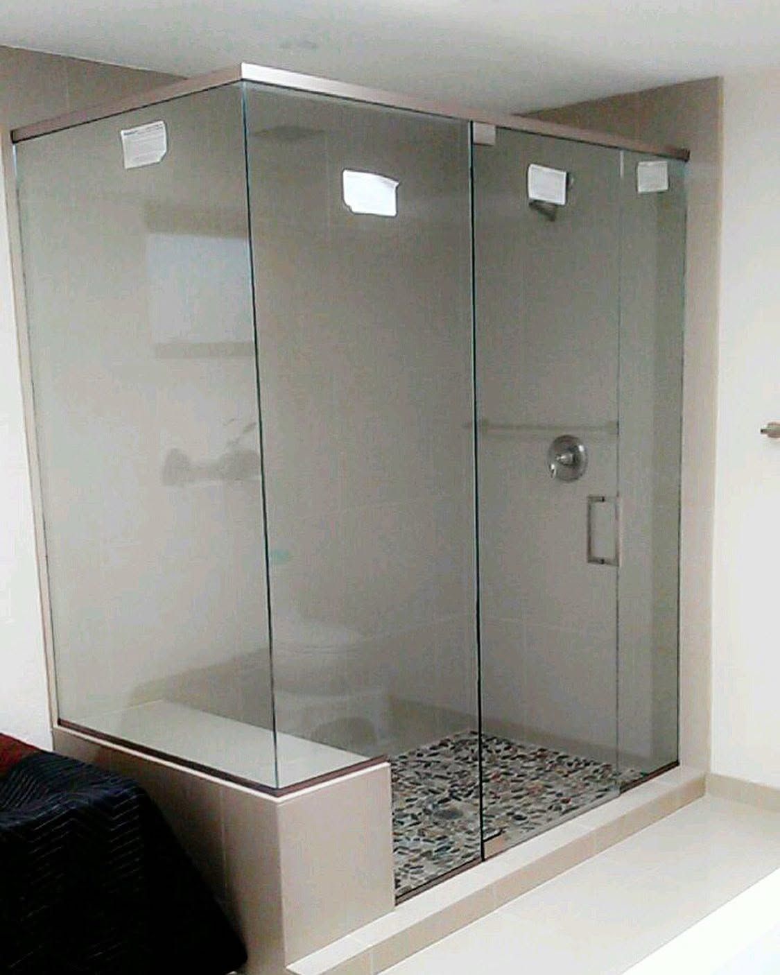 Glass shower enclosure in a tiled bathroom with frosted panels and a pebble floor.